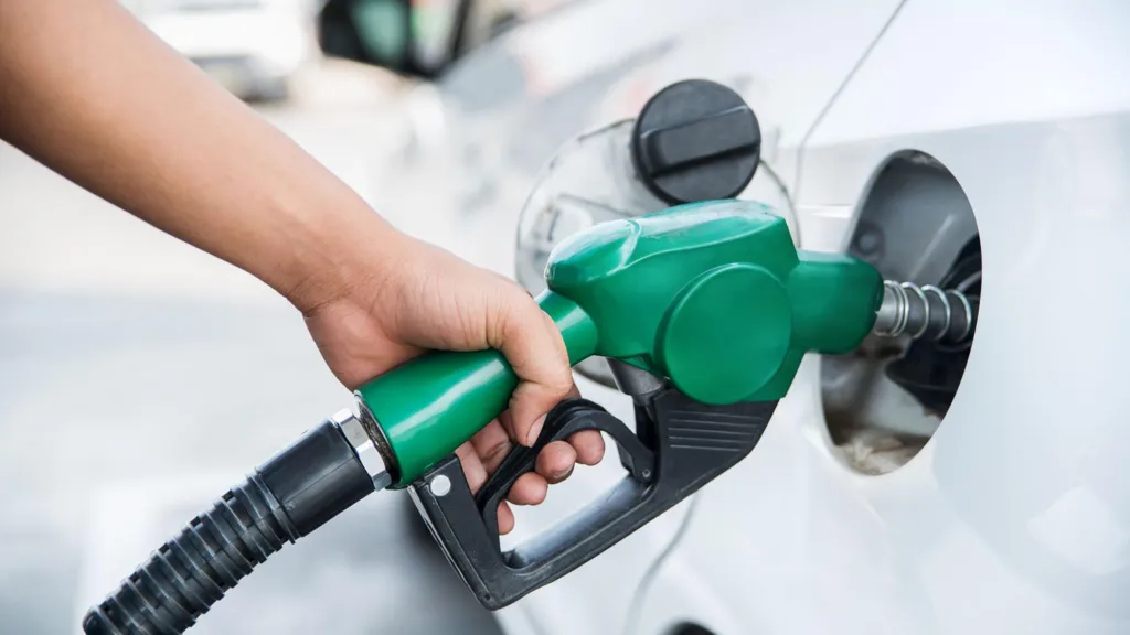 Person holding a petrol pump nozzle while filling a car at a fuel station.
